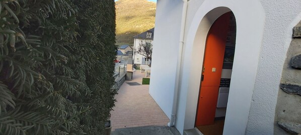 Un étroit sentier mène à un bâtiment à la façade blanche et à la porte orange.
