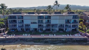 Un hotel de varios pisos con balcones, una zona de piscina y vistas a la playa y a las montañas.