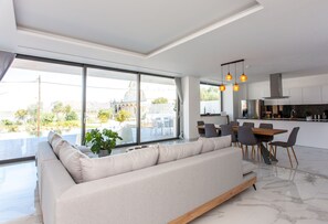 A modern living room with a large sofa, dining area, and kitchen. - Villa Valentina | Modern & Minimal Villa, Private Pool, Close To The Beach (Chania)