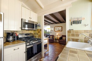 Una cocina con estufa, microondas y armarios. Hay una zona de comedor con mesa y sillas.