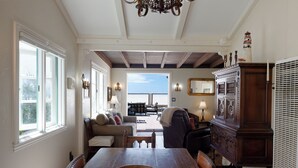 A dining area with a wooden table, chairs, a chandelier, and a view through a doorway. - 1205O Spanish Beach Bungalow Retreat (Oxnard)