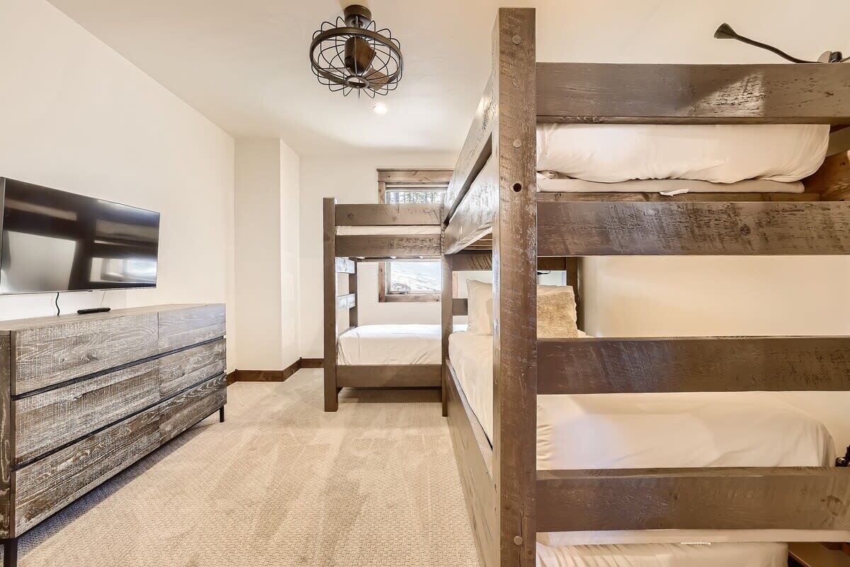 A bunk bed room with a TV on a wooden dresser, carpeted floor, and a hanging light fixture.