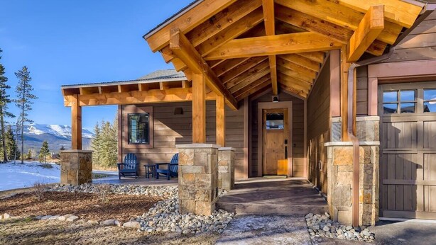 A wooden cabin with a covered porch, stone pillars, and a view of snow-capped mountains. - Modern Retreat | Views | Shuttle Stop (Breckenridge)