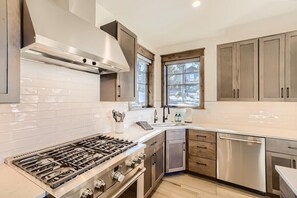 A modern kitchen with a gas stove, stainless steel appliances, wooden cabinets, and a window with a view.