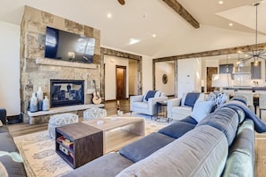 A spacious living room with a stone fireplace, a flat-screen TV, and a large sofa.