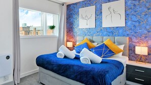 Et moderne hotelværelse med en stor seng, blå og gule puder, en grå sengegavl og to billeder på væggen.