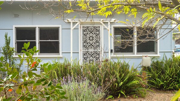 A house with a white door, two windows, and a garden with various plants.