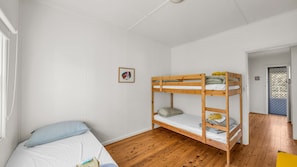 A room with a bunk bed, a single bed, a framed picture on the wall, and a door leading to another room.