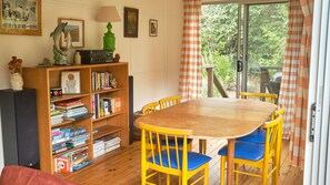 A room with a wooden table and chairs, a bookshelf with books, a lamp, and a window with curtains.