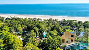 Vue aérienne d’une propriété située sur la côte, caractérisée par une végétation luxuriante, une plage et une piscine bien visible.