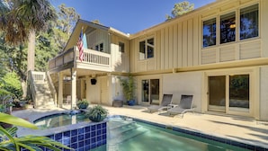 Une maison à deux étages dotée d’une piscine, d’un balcon et d’un patio aménagé avec des chaises longues.