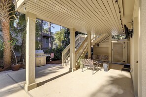 Eine überdachte Terrasse im Freien mit Grill, einer Holzbank und einer Treppe, die zu einer zweiten Ebene führt.