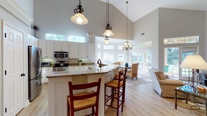 Una cocina amplia con armarios blancos, una isla grande y un comedor con sillas.