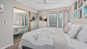 Ein Schlafzimmer mit einem Bett, einem Deckenventilator, einem Fernseher und einer Tür zu einem anderen Raum.