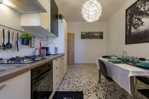 Uma cozinha moderna com fogão a gás, panelas penduradas, micro-ondas e uma área de jantar com mesa posta para quatro pessoas.