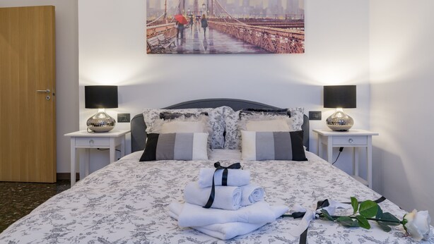 Hotellihuone, jossa on sänky, kaksi yöpöytää, sillan kuva ja kukallinen päiväpeite.