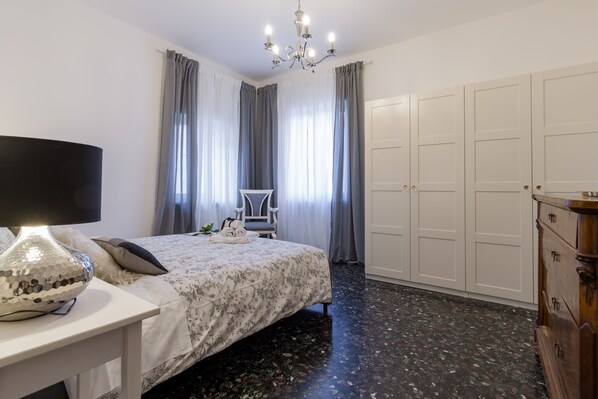 Um quarto com uma cama, uma escrivaninha com luminária, cômoda e guarda-roupa.
