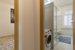 Uma casa de banho moderna com cabine de duche em vidro, máquina de lavar integrada e sanita.