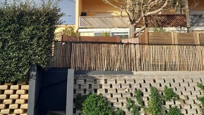 Un immeuble résidentiel doté d’un balcon, d’un escalier menant à un garage et d’une clôture en bambou.