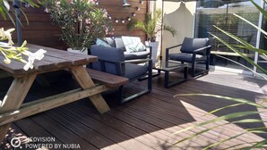 Une terrasse extérieure avec une table en bois, deux chaises, une petite table et un grand parasol pour faire de l’ombre.