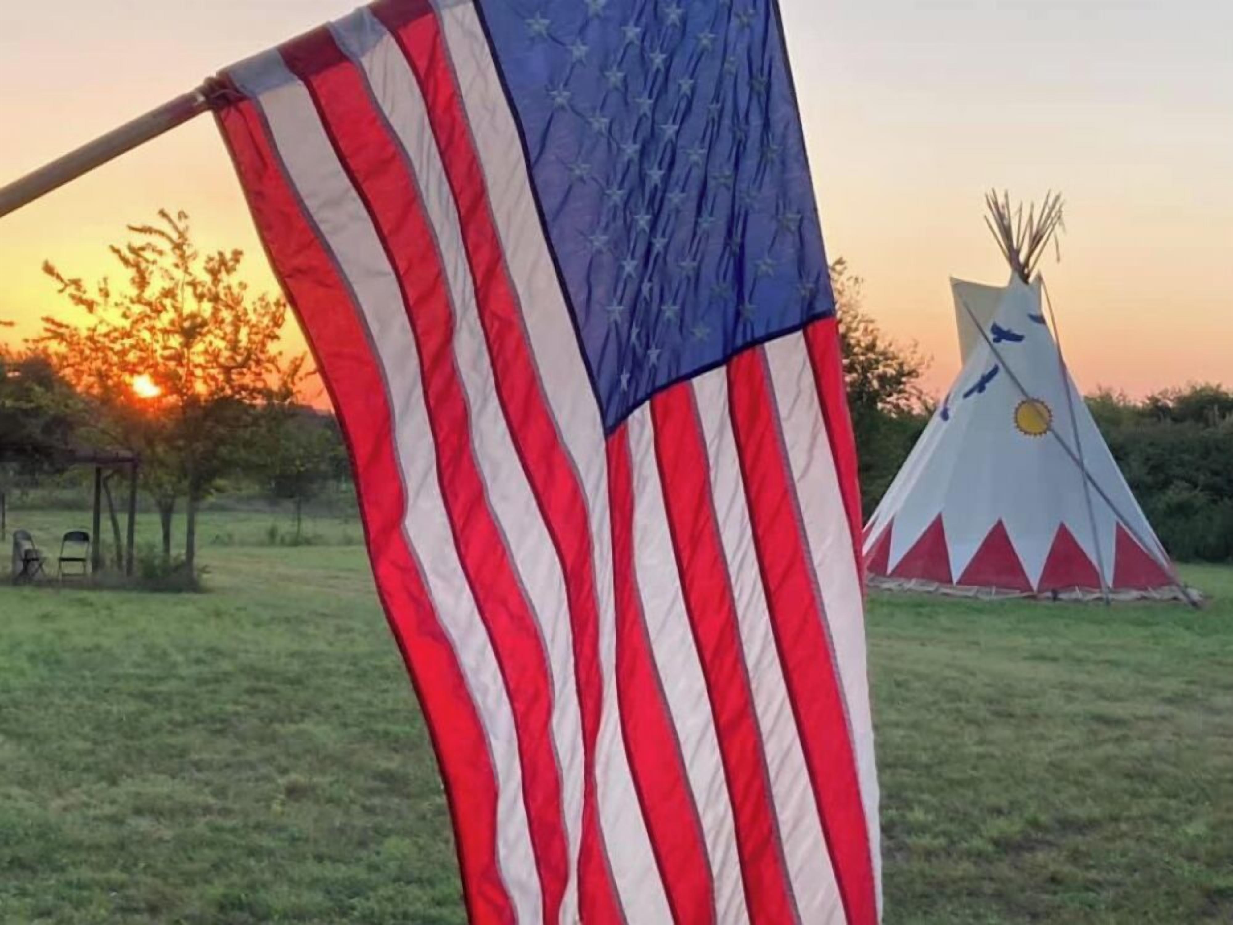A flagpole with an American flag, a teepee, and a sunset in the background.
