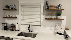 A modern kitchen with a stainless steel sink, white cabinetry, and decorative items on shelves.