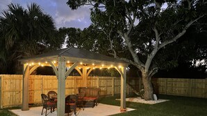A covered patio area with string lights, outdoor furniture, and a wooden fence.