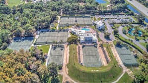 Vue aérienne d’un complexe sportif comprenant plusieurs courts de tennis, une piscine et des espaces verts environnants.