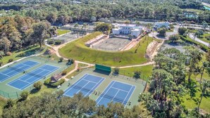 Vue aérienne d’un complexe de courts de tennis entouré d’arbres et d’immeubles.