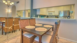 Un coin repas avec des chaises en osier et une table, une cuisine équipée d’un four à micro-ondes et un lustre.