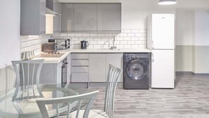 Eine moderne Küche mit Geschirrspüler, Waschmaschine und Essbereich mit einem Glastisch und Stühlen.