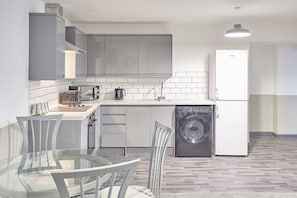 Enjoy meals at the glass dining table with four chairs, featuring a washing machine and refrigerator.