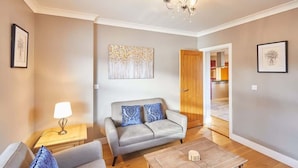 A living room with a grey sofa, a wooden coffee table, and a chandelier. There is a framed artwork on the wall and a door leading to another room. - Host & Stay | Holmedene (Filey)