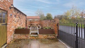 A brick building with a wooden door, a small patio with a table and benches, and a black metal fence. - Host & Stay | Holmedene (Filey)