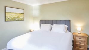 A neatly made bed with a grey headboard, a bedside table with a lamp, and a framed picture of a field on the wall. - Host & Stay | Holmedene (Filey)