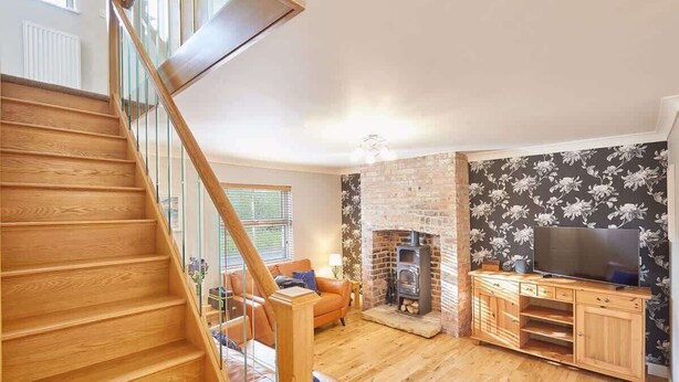 A wooden staircase leading to a living room with a fireplace, a television on a wooden cabinet, and a floral wallpaper. - Host & Stay | Holmedene (Filey)