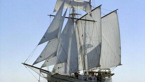 Un barco de vela con varias velas, una cabina y cubierta con gente.
