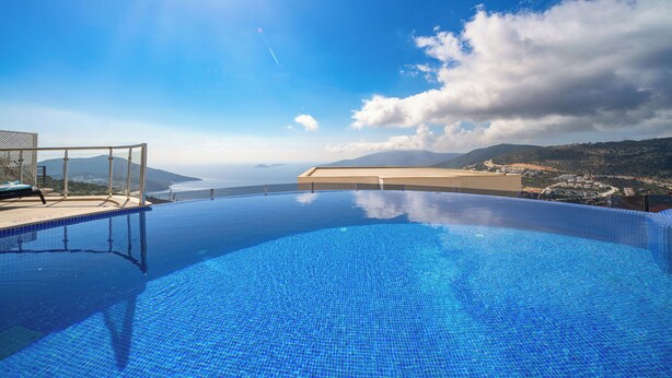 Une magnifique piscine à débordement d’un bleu profond, offrant une vue sur l’océan et les montagnes.
