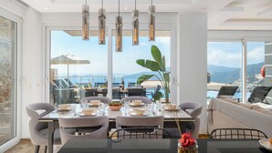 Un coin repas avec une table dressée pour quatre personnes, de grandes fenêtres et une vue sur la mer.