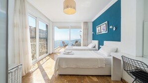 Une chambre d’hôtel avec deux lits, un balcon offrant une vue, un luminaire au plafond et un mur décoré de tableaux encadrés.