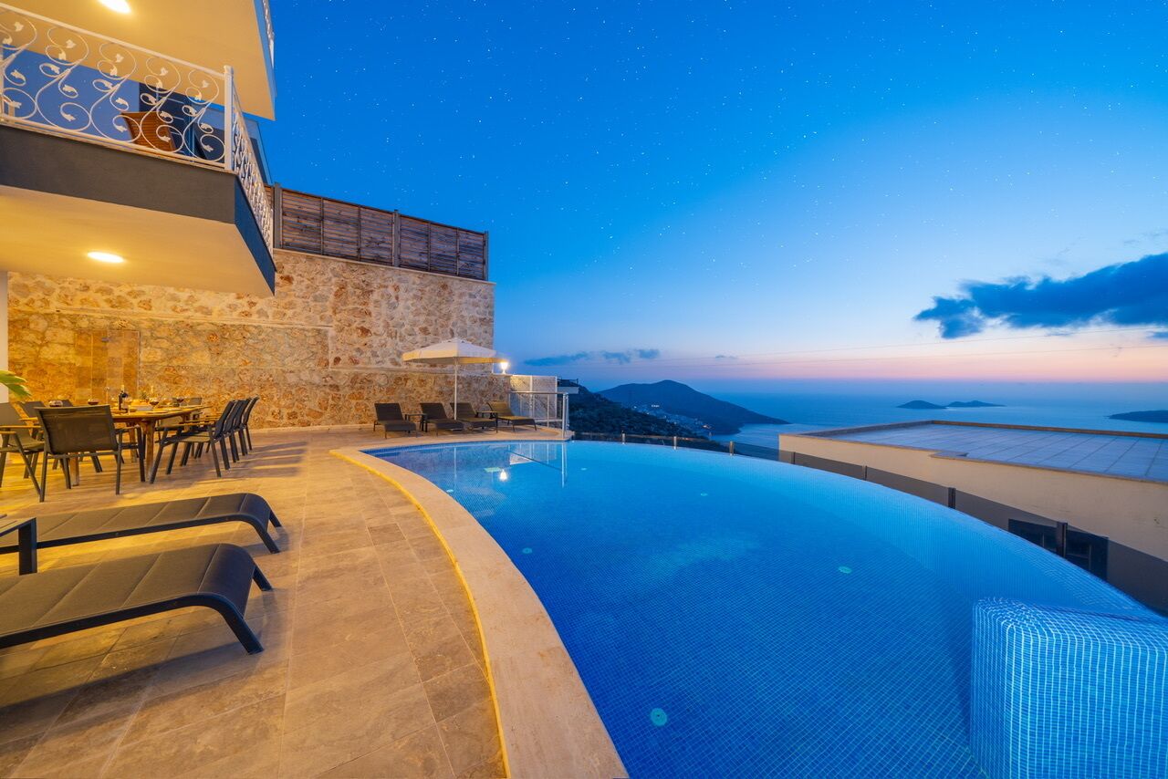 A infinity pool with a view of the sea and mountains at dusk.
