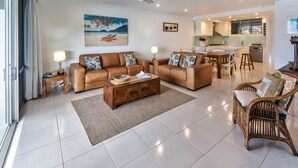A spacious living room with leather sofas, a wooden coffee table, and a dining area with a kitchen in the background. - Frangipani Lodge 203, Frangipani Lodge 203 (Hamilton Island)