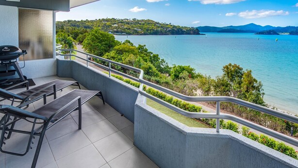 A balcony with a view of a lake, a grill, and outdoor seating. - Frangipani Lodge 203, Frangipani Lodge 203 (Hamilton Island)