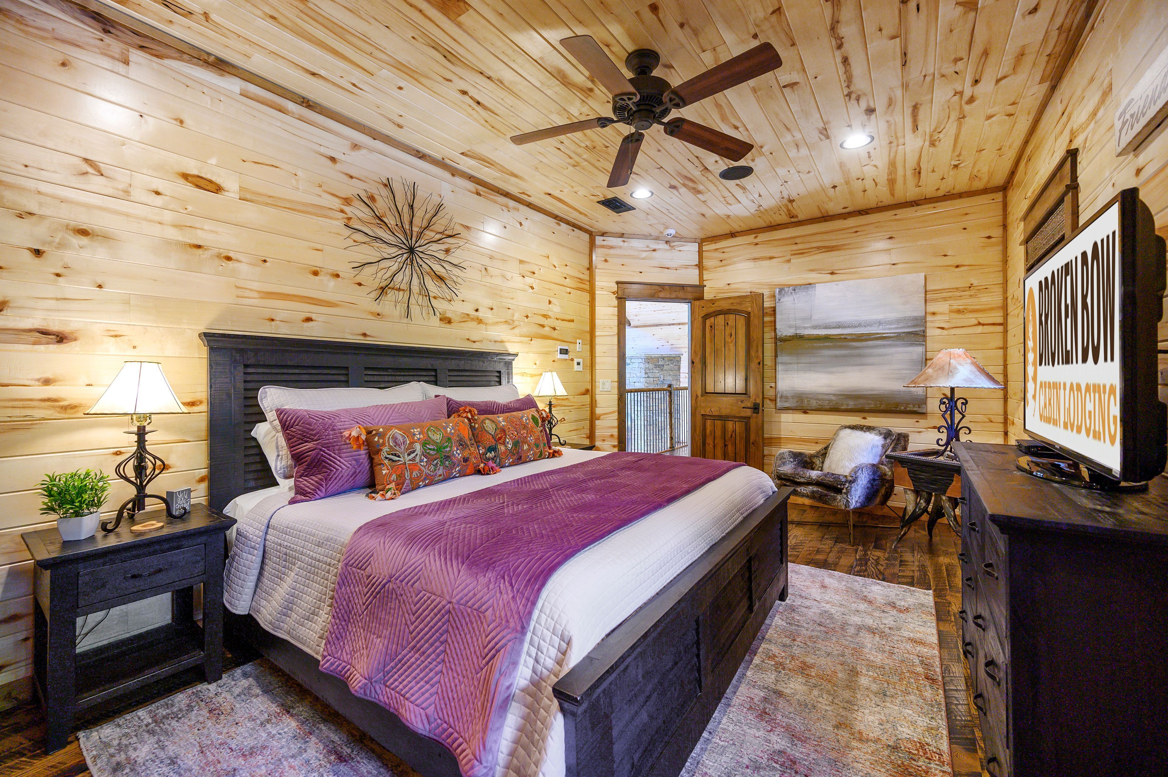 A wooden cabin bedroom with a bed, nightstands, a ceiling fan, and a television.