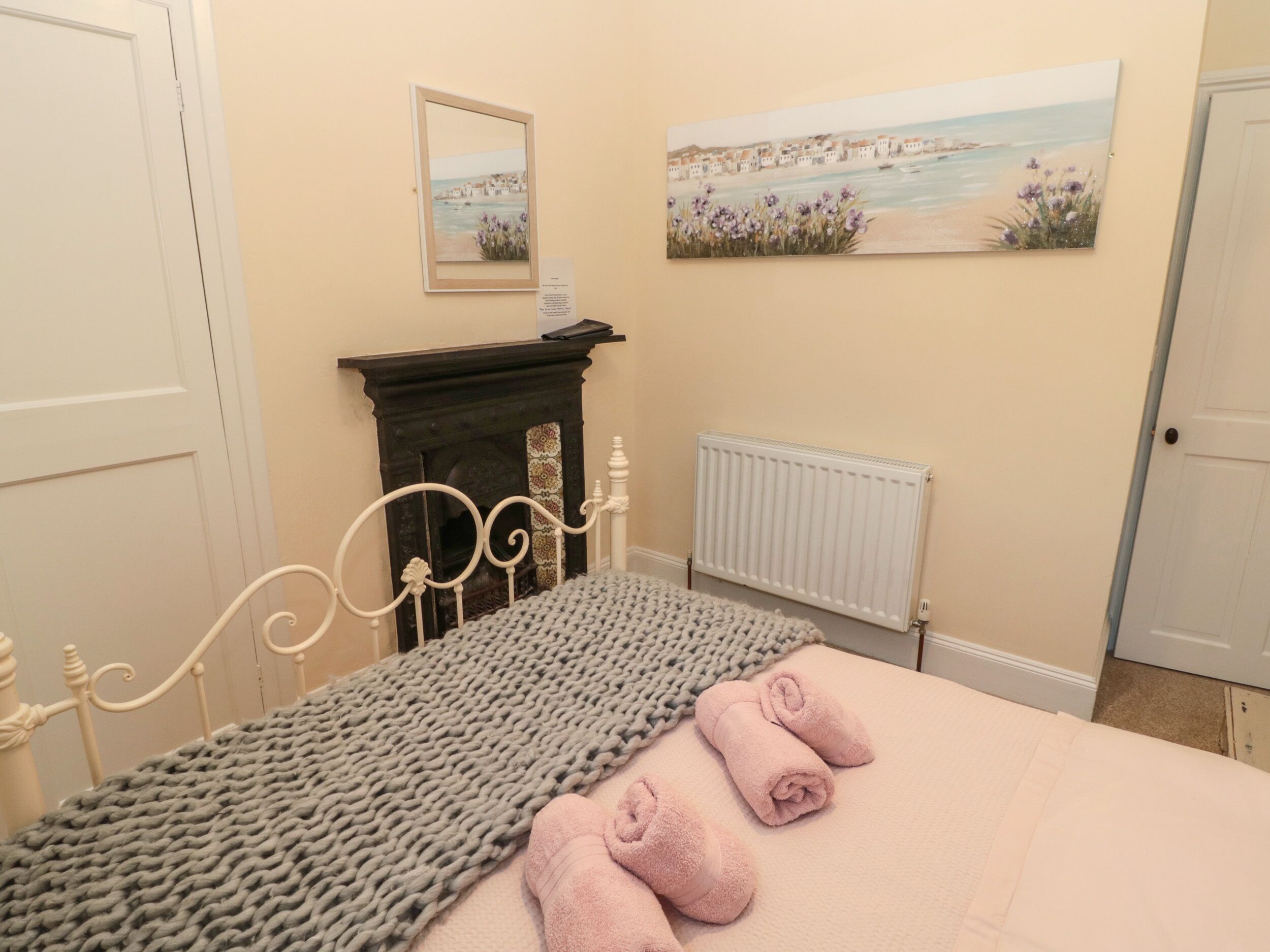 A bedroom with a bed, a fireplace, a radiator, and two paintings on the wall.