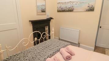 A bedroom with a bed, a fireplace, a radiator, and two paintings on the wall.