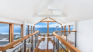 Un balcón amplio con vista al mar, barandillas de madera y un ventilador de techo.