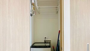 Un cuarto de lavandería con lavadora, tendedero y una escoba apoyada en la pared.