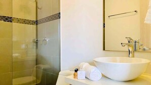 Un baño moderno con cabina de ducha de vidrio, inodoro blanco, lavamanos grande de color blanco y espejo sobre el lavamanos.