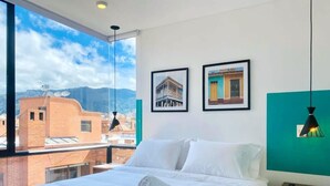Habitación de hotel con una cama grande, vista de edificios a través de una ventana y dos cuadros en la pared.